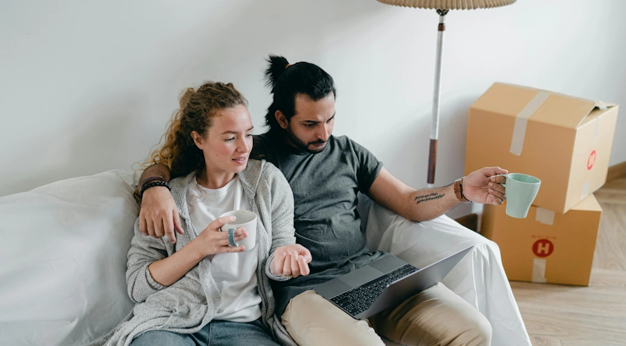 młode małżeństwo analizuje raport wyceny mieszkania online, siedząc na kanapie w trakcie przeprowadzki